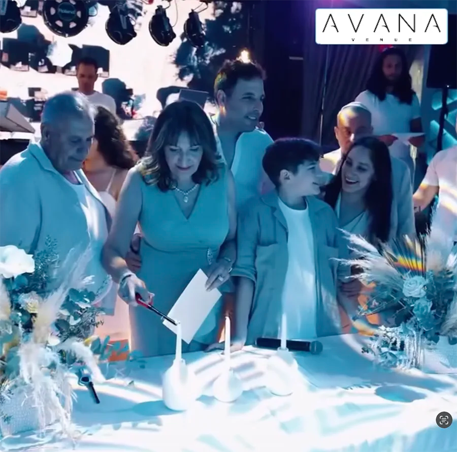 A group of people, including adults and a child, stand together smiling and lighting candles at a decorated table during a celebration. The AVANA Voyage logo is visible in the top right corner.